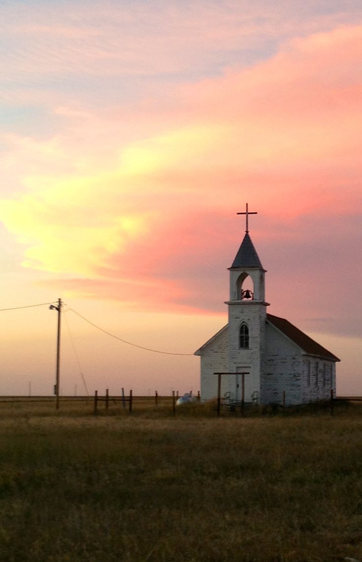 an old church sits in the middle of a grassy field with a sunset behind it