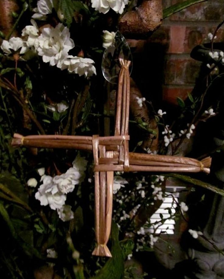 a cross made out of wicker sitting in front of some white flowers and greenery