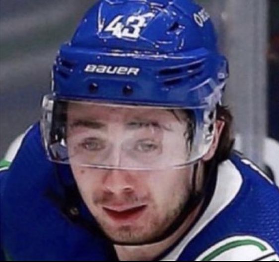 the hockey player is wearing a blue uniform and looking to his left with one eye open