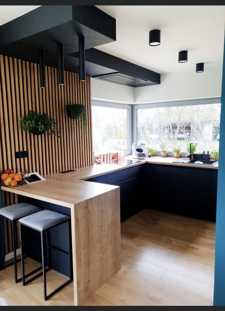 a modern kitchen with black cabinets and wood paneling on the wall, along with two stools