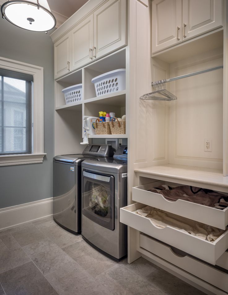 a washer and dryer in a small room with white cabinets, drawers and shelves