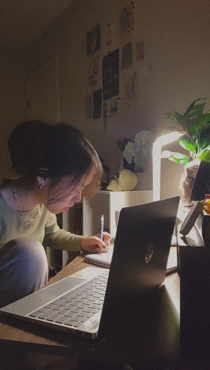 a woman sitting in front of a laptop computer on top of a wooden desk next to a plant