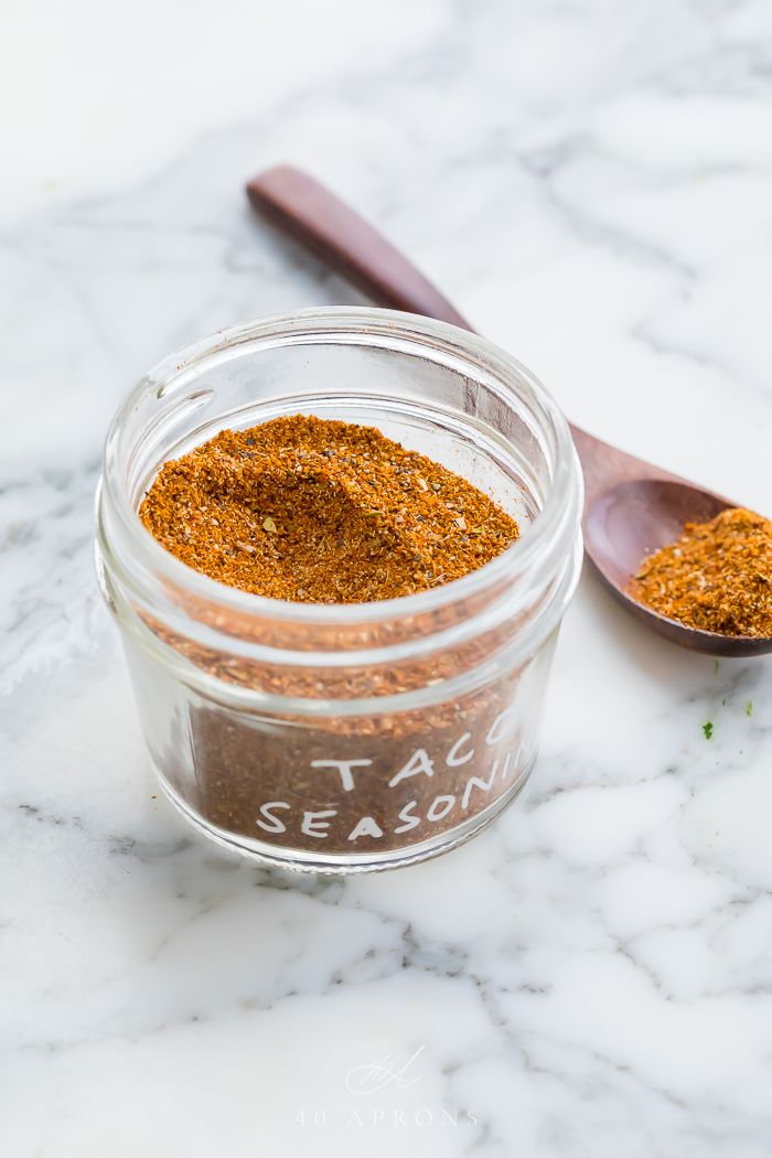 a glass jar filled with taco seasoning next to a spoon on a marble surface