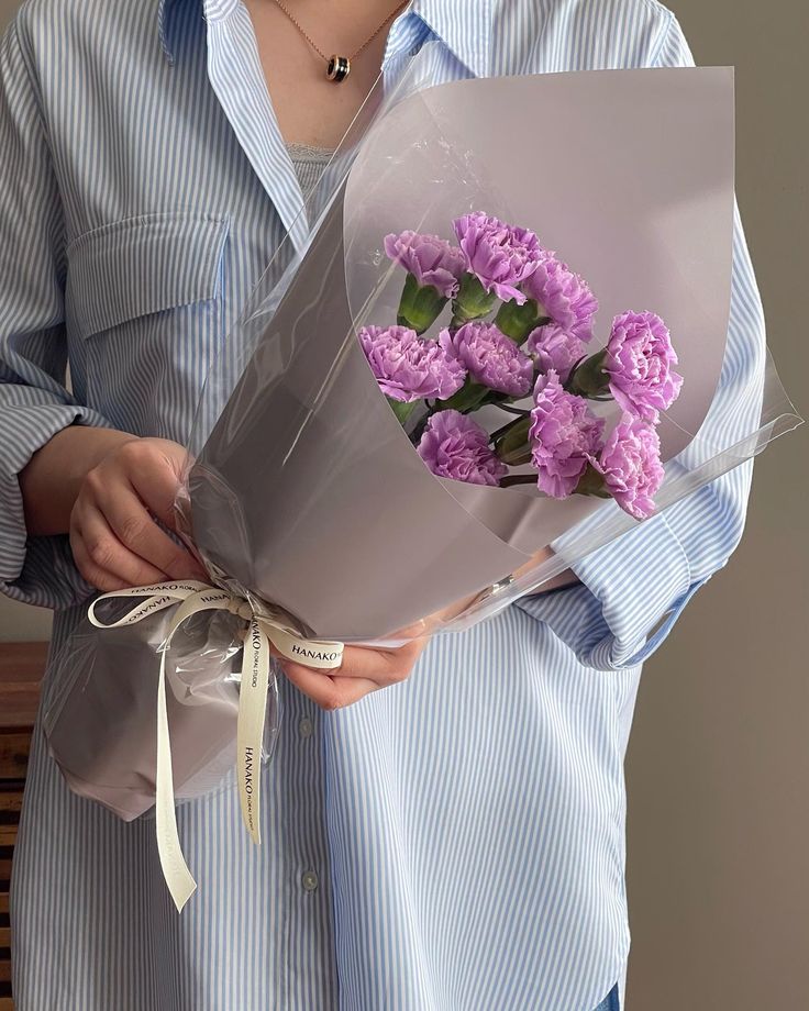 a woman holding a bouquet of purple flowers in her left hand and wearing a blue shirt