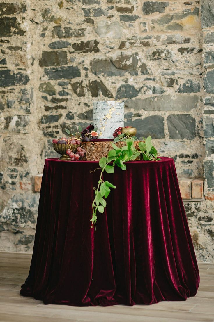 a wedding cake sits on top of a red velvet tablecloth with greenery around it