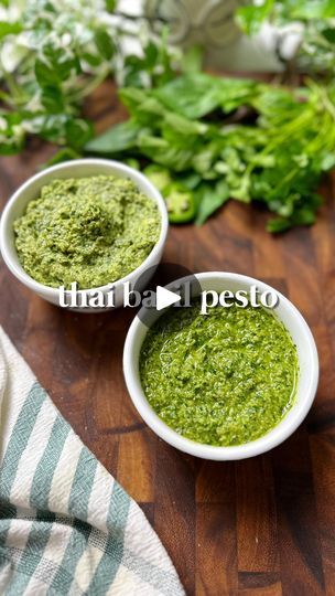 two white bowls filled with pesto sitting on top of a wooden table next to herbs