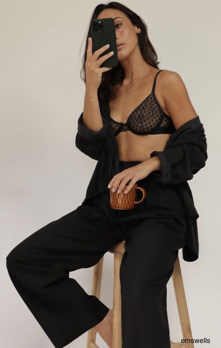 a woman sitting on a stool taking a selfie with her cell phone and holding a basket