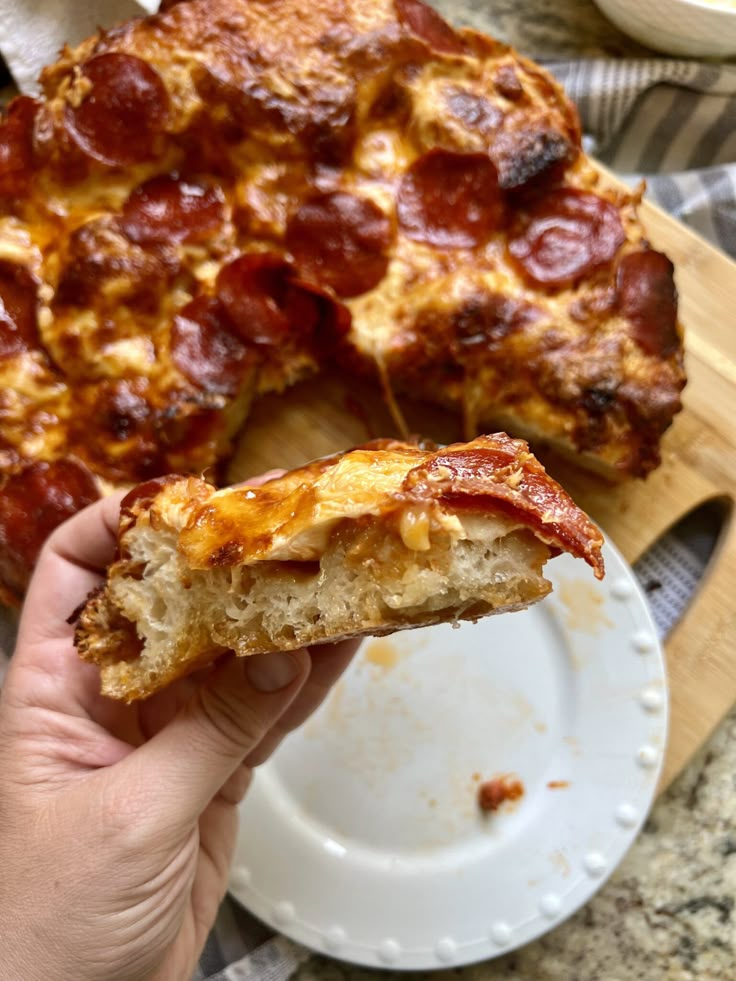 a person holding a piece of pizza in front of a partially eaten pizza on a plate