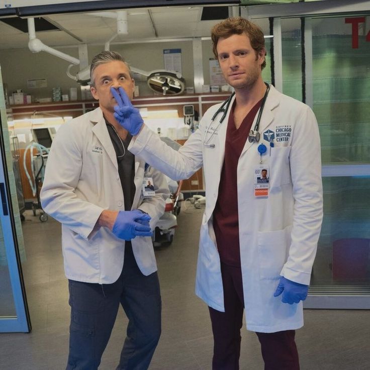 two men in white lab coats and blue gloves standing next to each other with their hands together