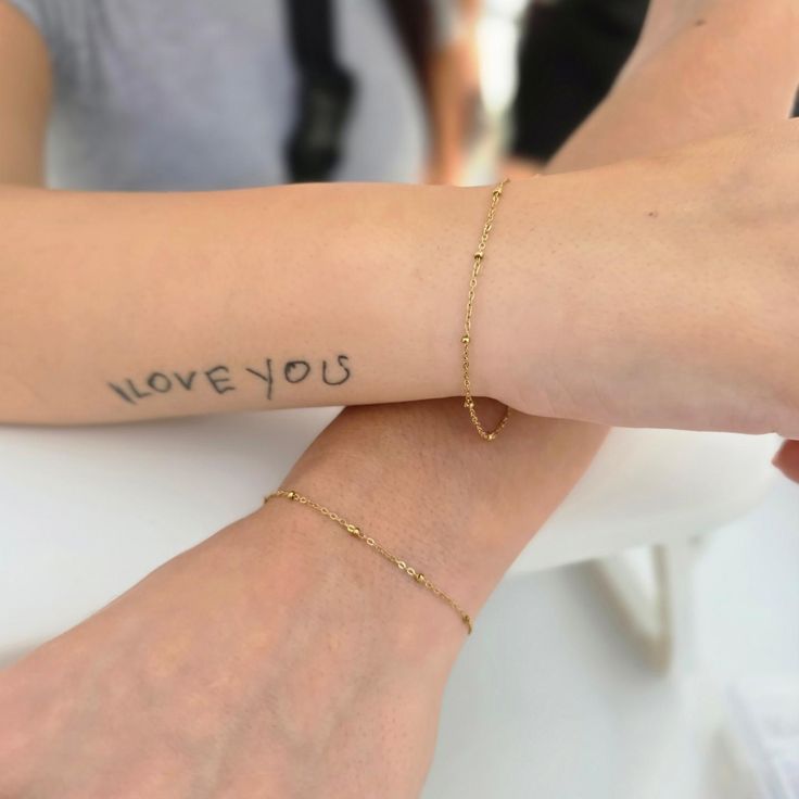 two people with tattoos on their arms sitting at a table and one is holding the arm of another person