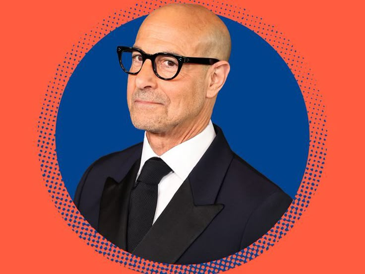 a bald man wearing glasses and a suit in front of an orange background with blue circles