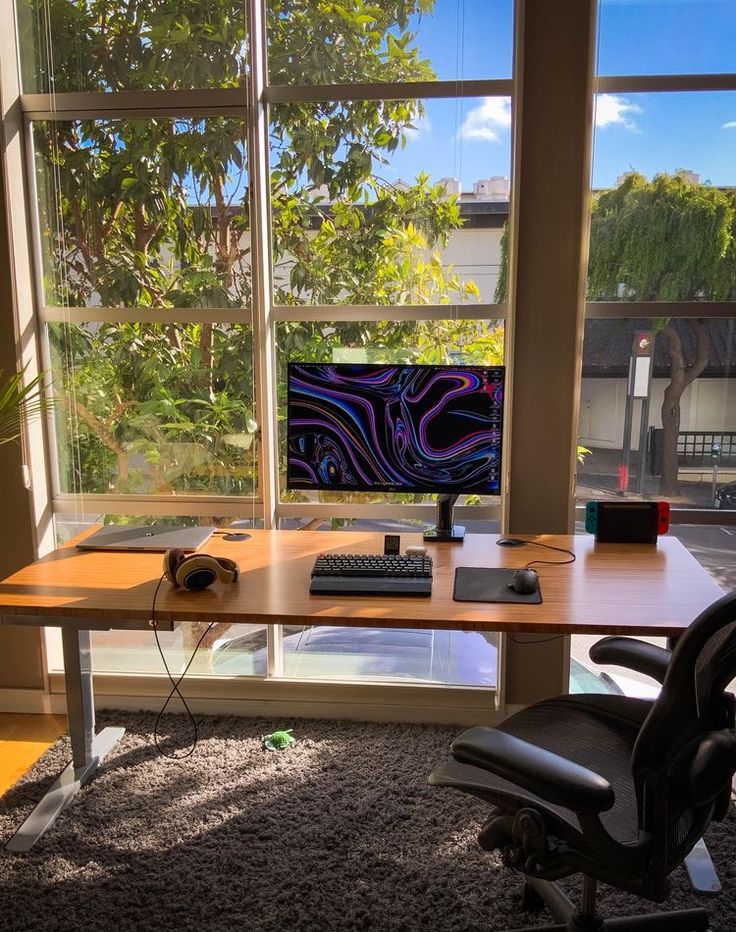 a desk with a computer on it in front of large windows