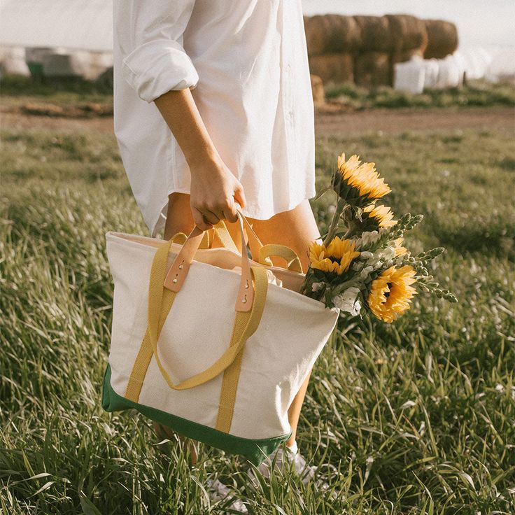 a woman is holding a bag and flowers in her hand while walking through the grass