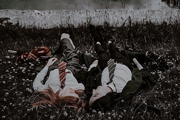 two people laying in the grass with their heads on each other's backs, one wearing a tie