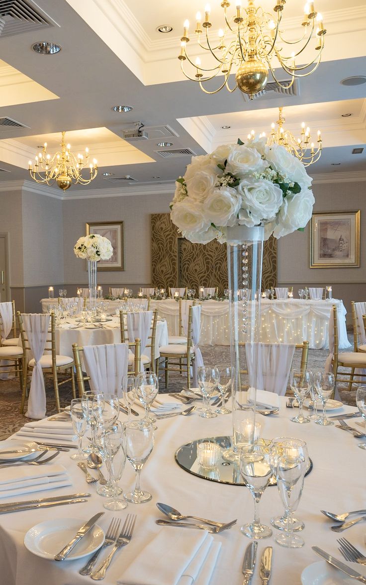 the centerpieces are set up for a formal function in this elegant room with chandeliers and white flowers