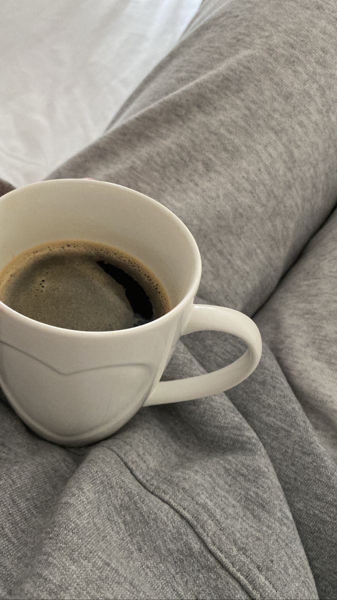 a cup of coffee sitting on top of a bed next to a pillow and blanket