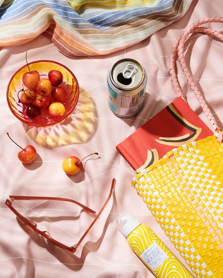 the contents of a purse are laid out on a pink blanket, including cherries and sunglasses