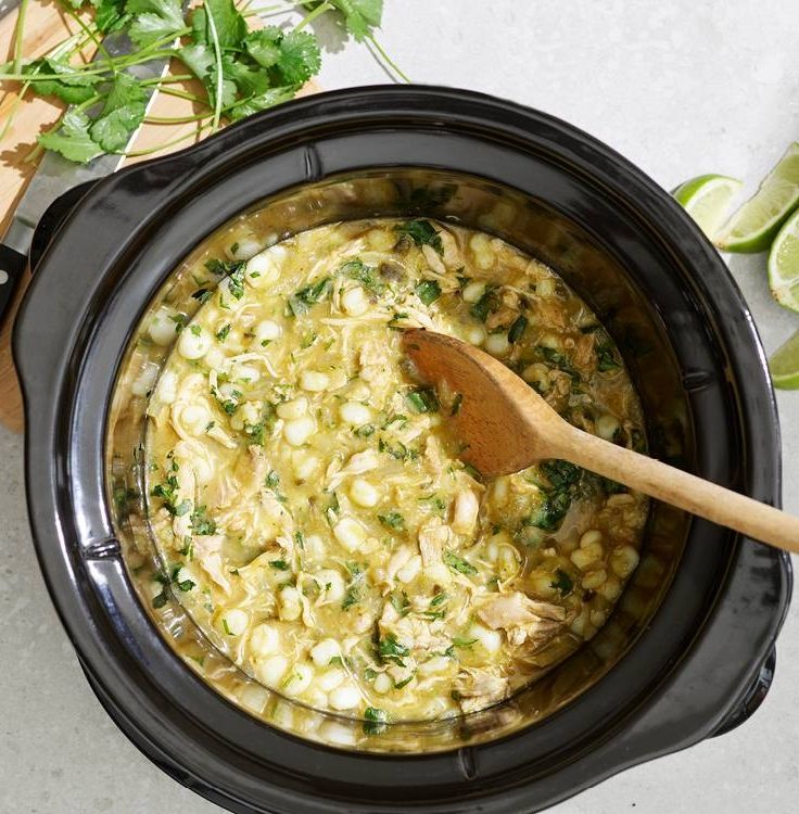 a crock pot filled with chicken and rice next to a wooden spoon on a table