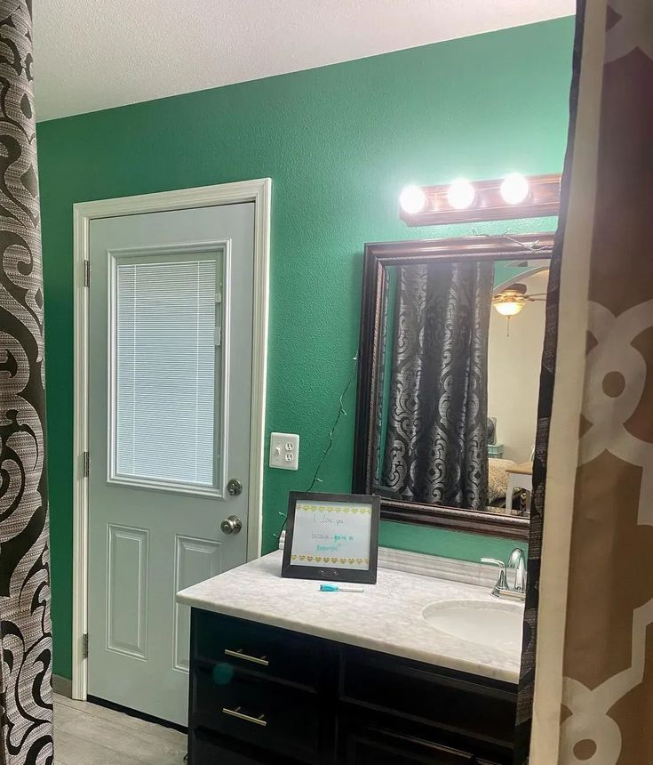 a bathroom with green walls and a white sink under a mirror next to a door