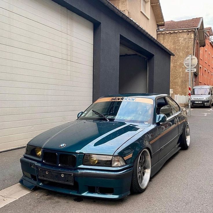 a blue car parked in front of a garage door on the side of a street