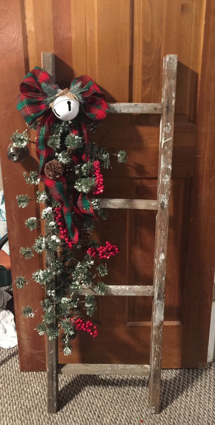 a wooden ladder with a christmas wreath hanging on it's side and a teddy bear in the middle