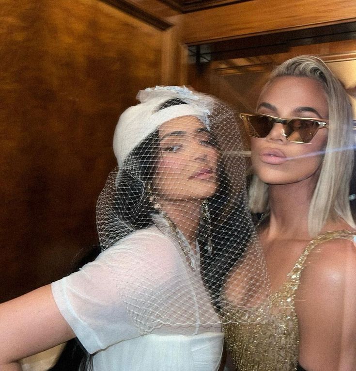 two women dressed in white and gold posing for the camera with one wearing a veil over her head