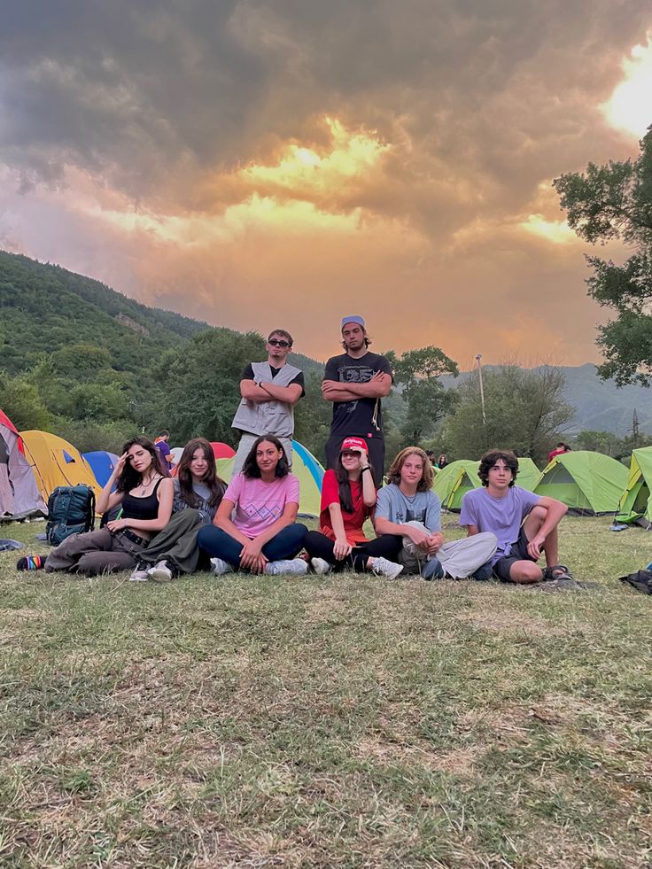 a group of people sitting on the ground in front of tents under a cloudy sky