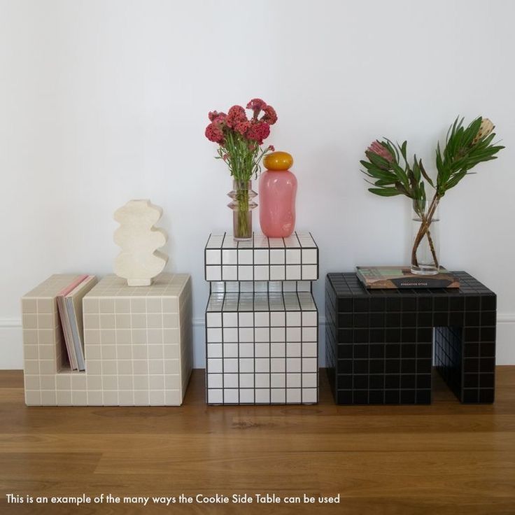 three vases with flowers and books on top of them in front of a white wall