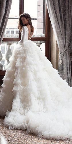 a woman standing in front of a window wearing a wedding dress with ruffles