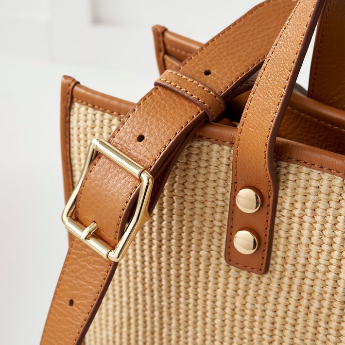 Crafted from a durable raffia-inspired fabric and high quality leather, our Essential Raffia Tote features a spacious, open-tote design with leather carry handles and an adjustable leather crossbody strap that can be swapped out for one of our colorful straps to create your own style. Add an embroidered monogram to add a personal touch to your new everyday tote.    15"w x 5"d x 12.5"h  Faux raffia with leather side panels and a soft linen lining.  Spot clean only with damp cloth.  Please see Pro Versatile Straw Satchel Bag With Adjustable Strap, Light Brown Leather-handled Bucket Tote Bag, Versatile Beige Straw Bag With Double Handle, Everyday Leather Straw Bag With Detachable Strap, Leather Straw Bag With Detachable Strap For Everyday Use, Modern Natural Bucket Bag With Adjustable Strap, Square Straw Bag With Detachable Strap For Travel, Leather Straw Bag With Detachable Strap And Double Handle, Light Brown Rectangular Shoulder Bag With Leather Handles