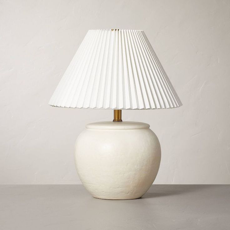 a white table lamp with a gold base and pleated lampshade on top