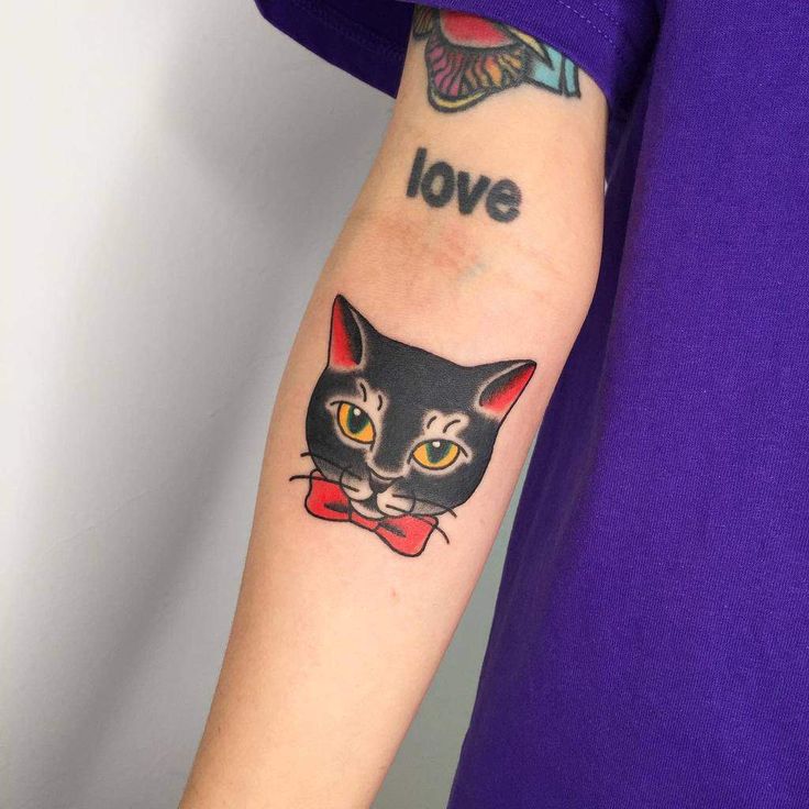 a black cat with yellow eyes and a bow tie tattoo on the left arm is shown