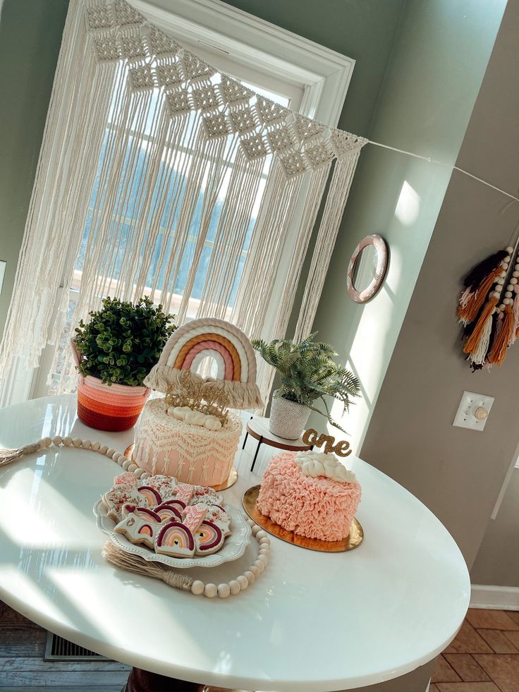 a table with two cakes on it in front of a window and potted plants