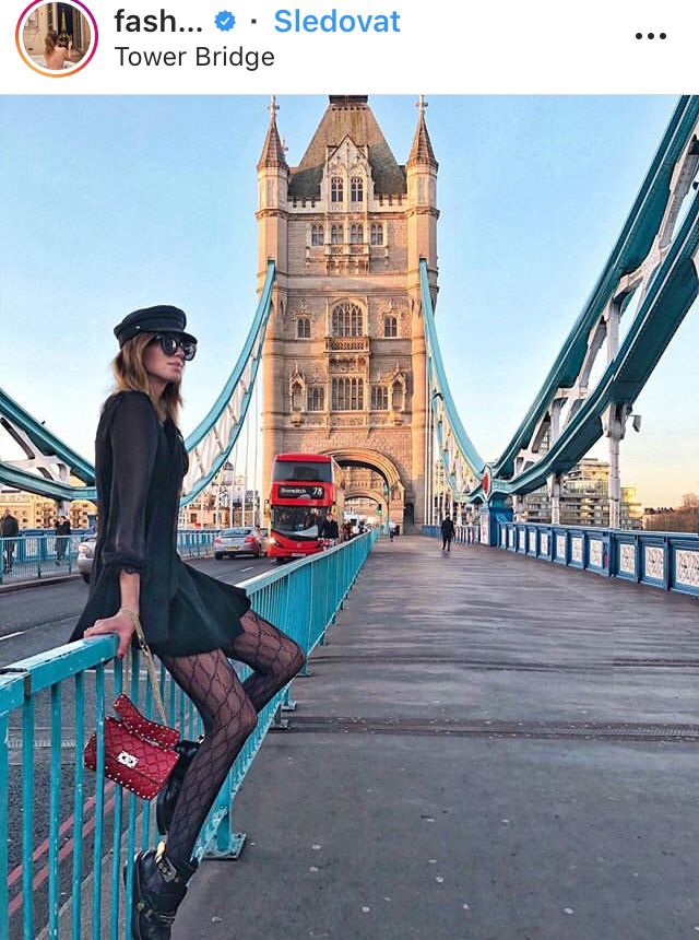 a woman standing on the side of a bridge next to a red bag and a bus