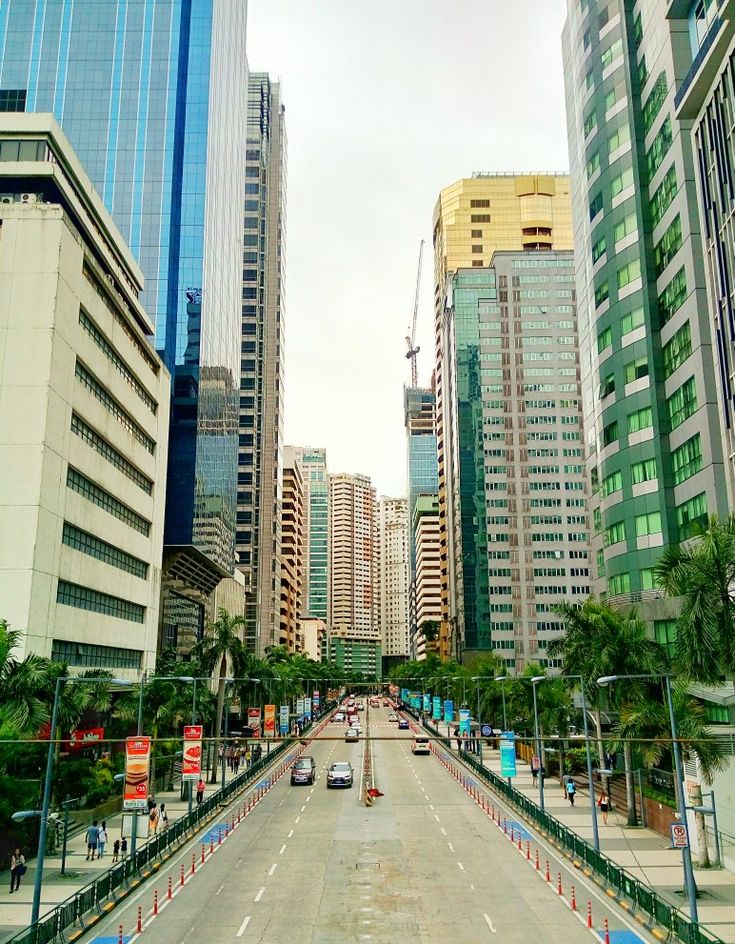 an empty city street with tall buildings in the back ground and cars driving down it