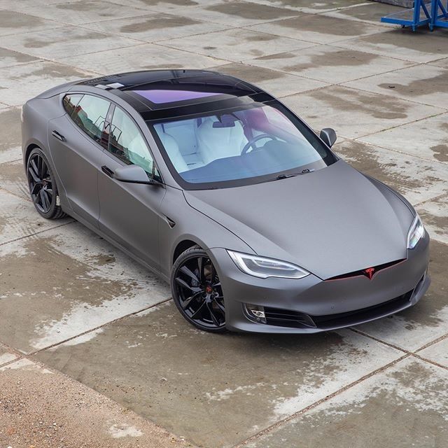 a grey tesla model s parked in front of a parking lot with no one around