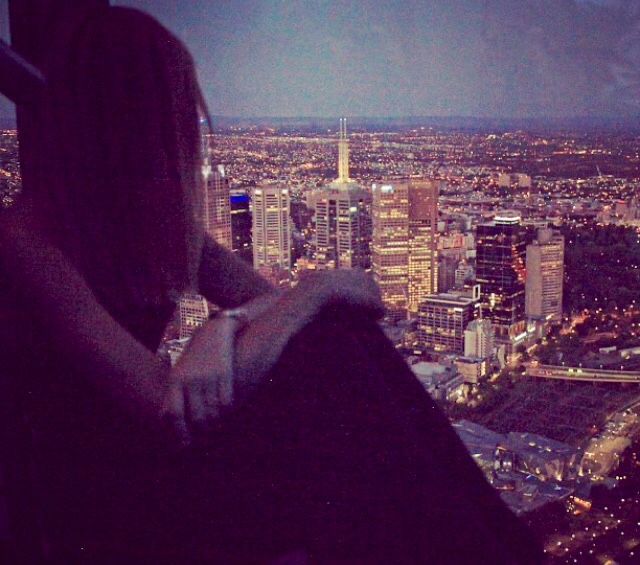 a man sitting on top of a tall building next to a cityscape at night