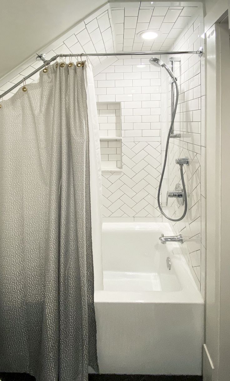 a white bath tub sitting under a bathroom window next to a shower curtain and rug