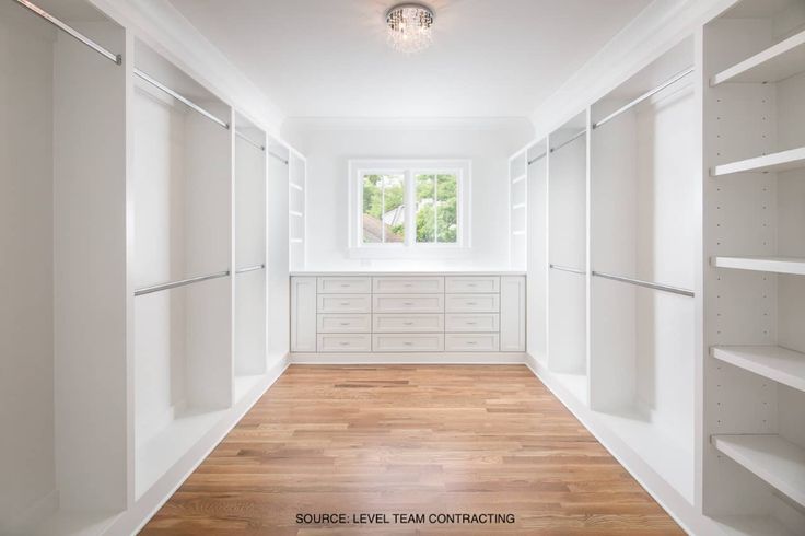 an empty walk in closet with white walls and shelves on each side, along with wooden flooring