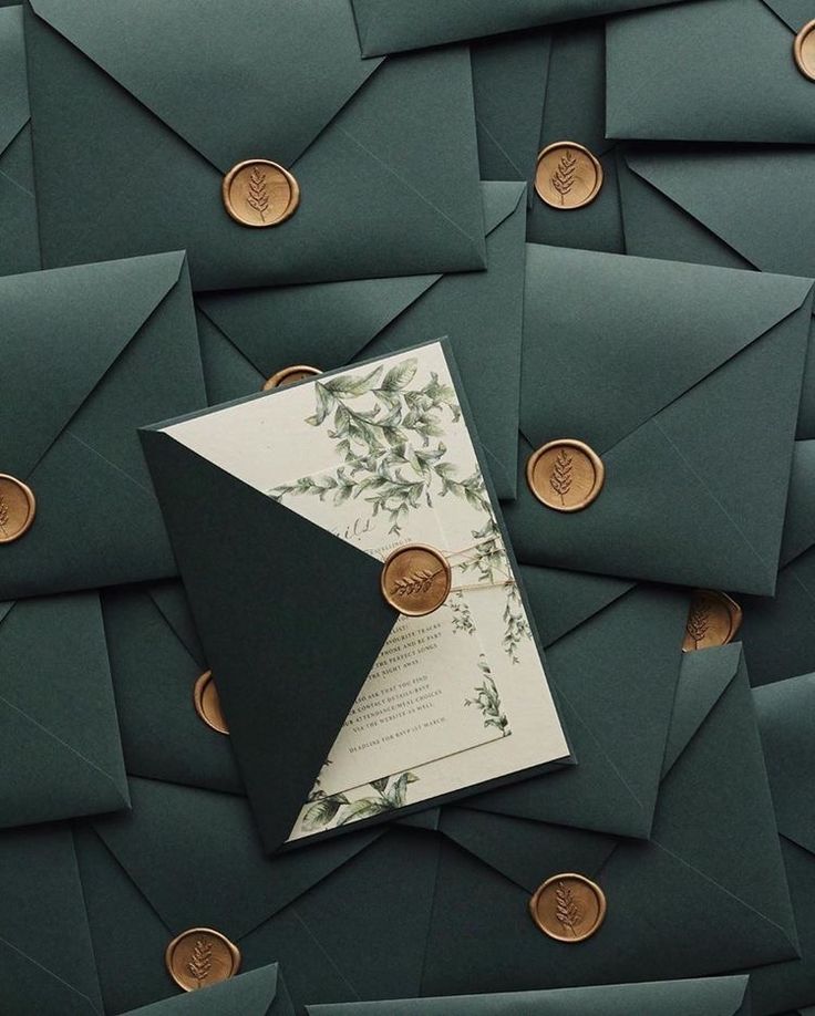 green envelopes with gold buttons and a wedding card in the middle, surrounded by other dark green envelopes