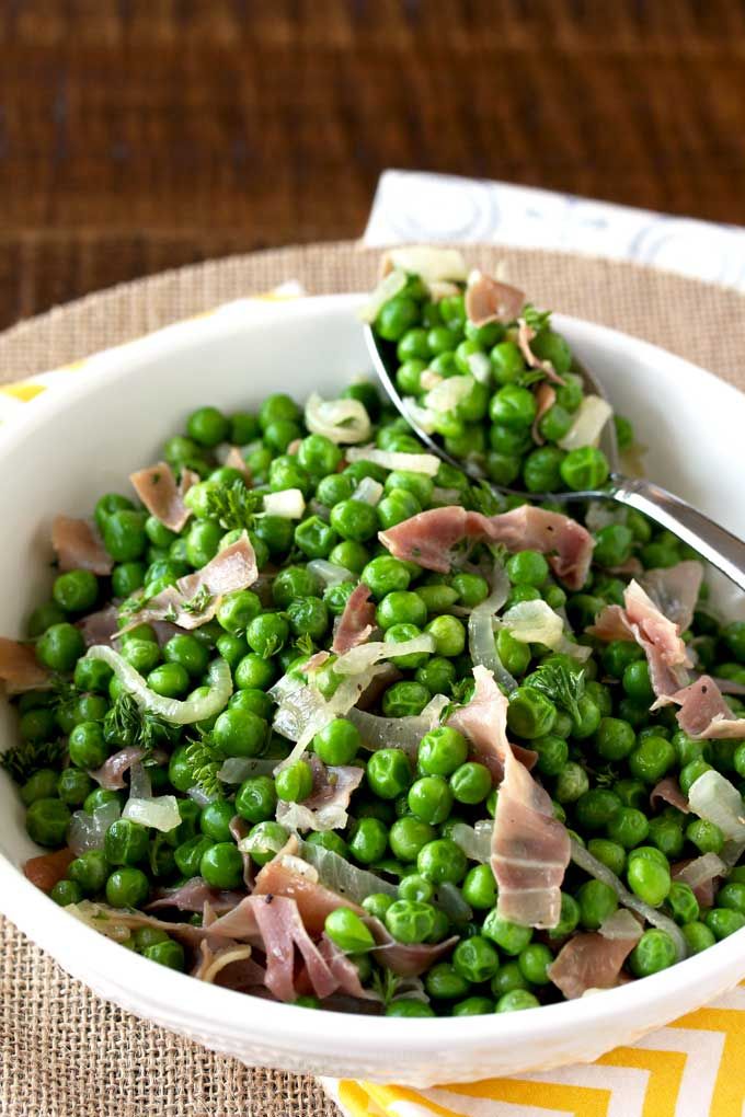 a bowl filled with peas and ham on top of a yellow table cloth next to a fork