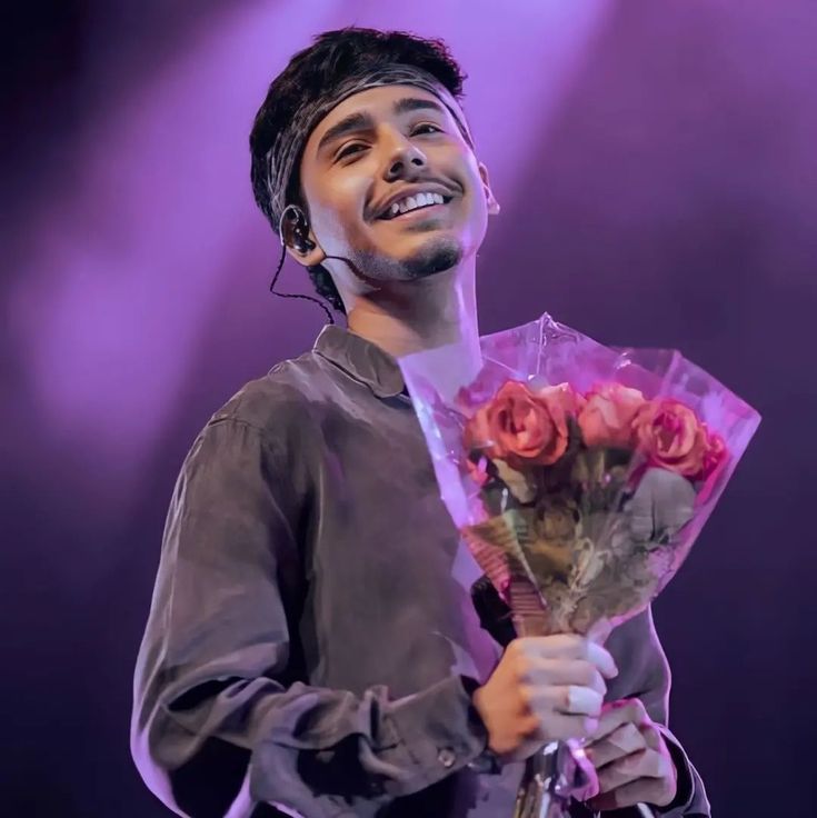 a man holding a bunch of flowers on top of a purple stage background with spotlights