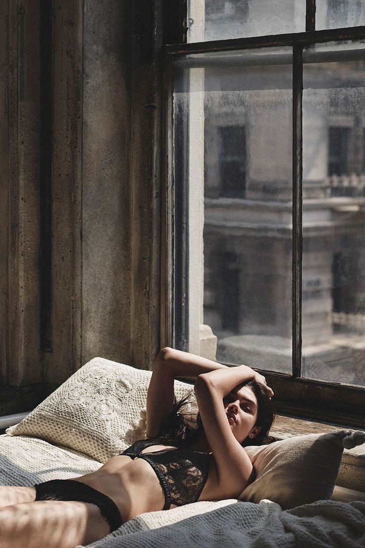 a woman laying on top of a bed in front of a window next to a pillow