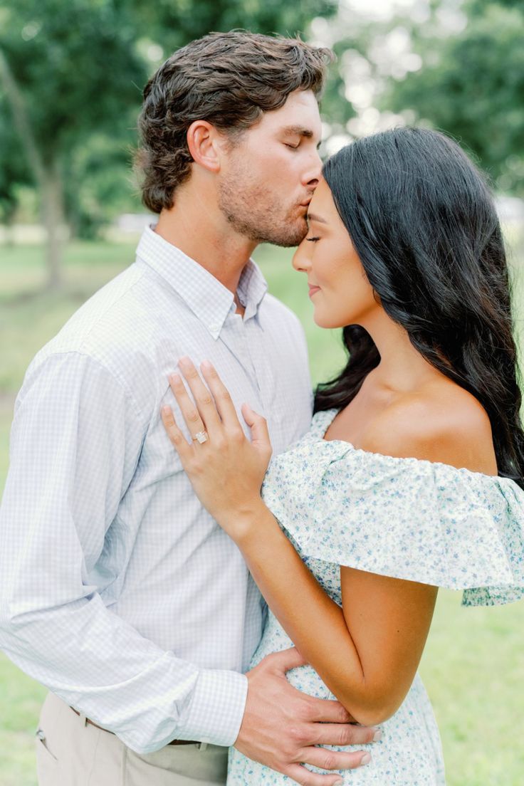 a man and woman are kissing in the park while holding each other's hands