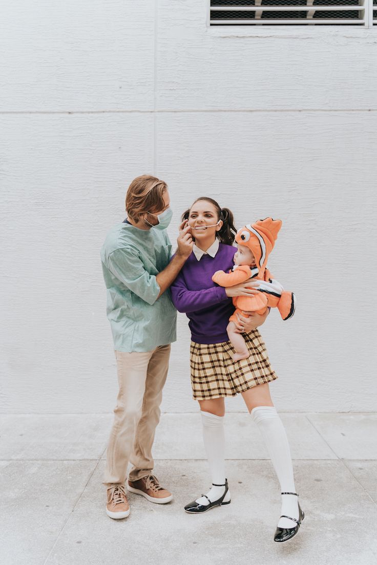 a man and woman standing next to each other holding an orange stuffed animal in front of a white wall