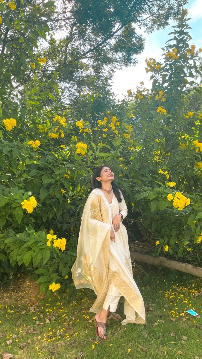 a woman is standing in the grass near some yellow flowers and trees with her eyes closed