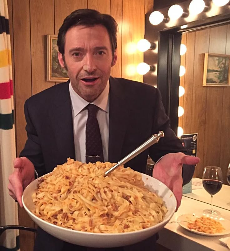 a man in a suit and tie holding a bowl of noodles with a fork on it