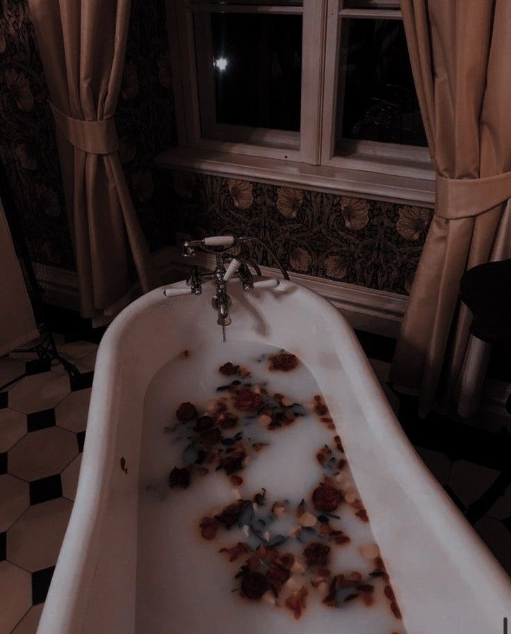 a bathtub filled with rose petals and water in front of a window at night