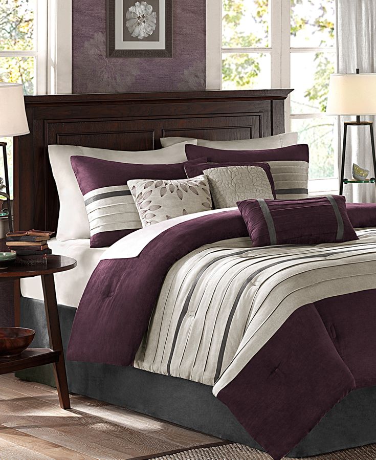 a bed with purple and white comforters in a bedroom next to a night stand