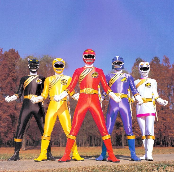 five different colored power rangers standing in front of some trees and grass with their hands on their hipss